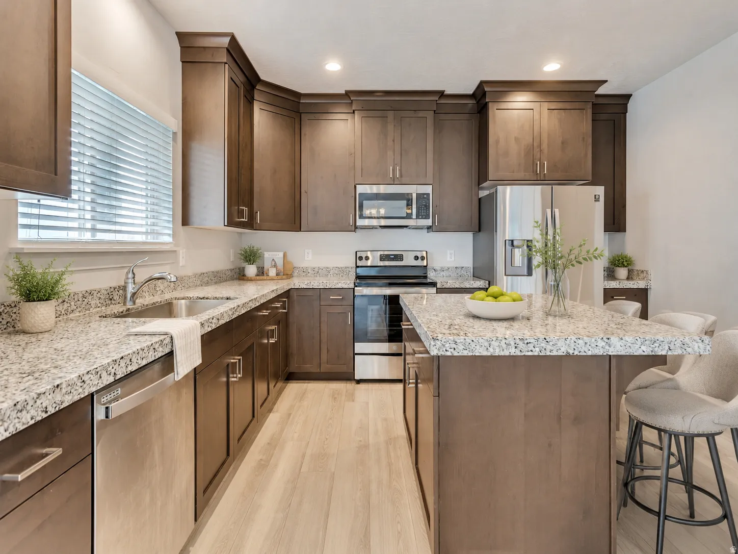 Kitchen featuring wood-finish cabinetry, light-toned wood-finish flooring, stainless steel appliances, a kitchen island with seating, and stone countertops