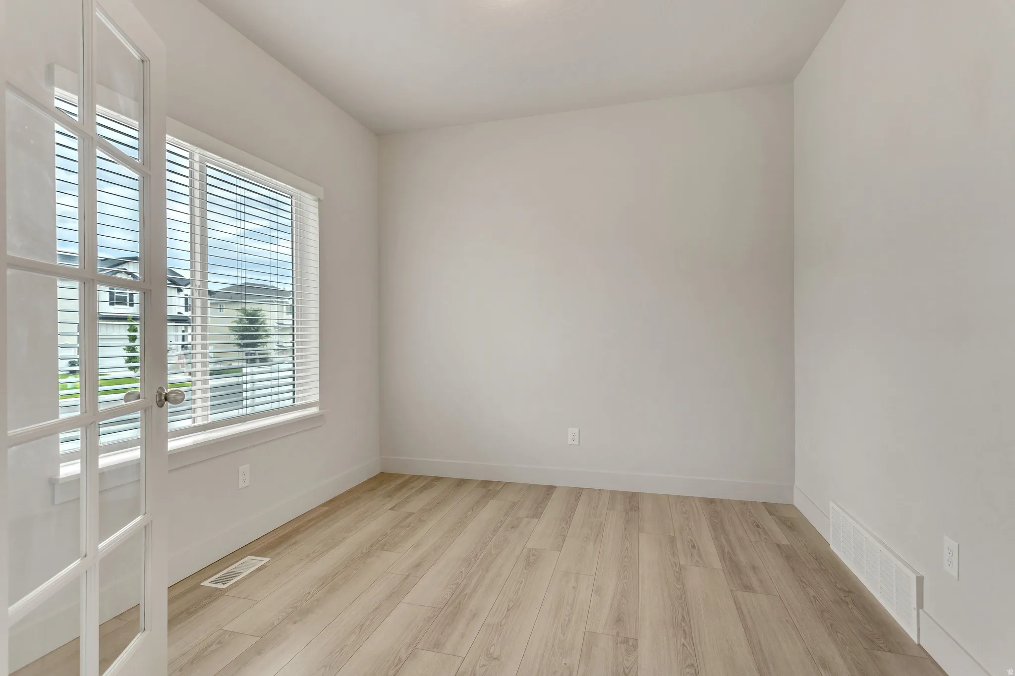 Light wood-finish flooring, white walls, and a large window with horizontal blinds