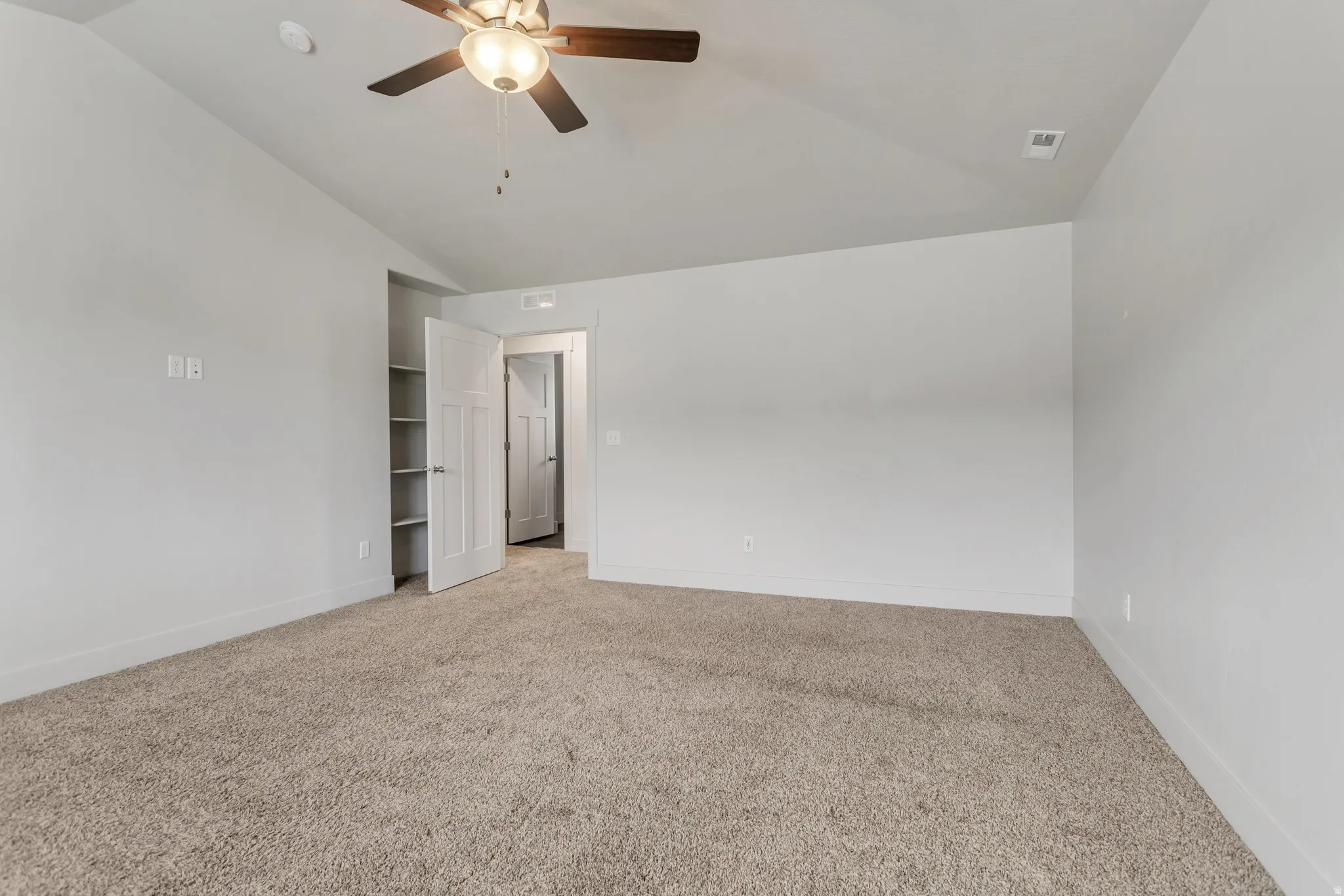 Carpeted room featuring a vaulted ceiling, ceiling fan with light fixture, built-in shelving, and white interior doors