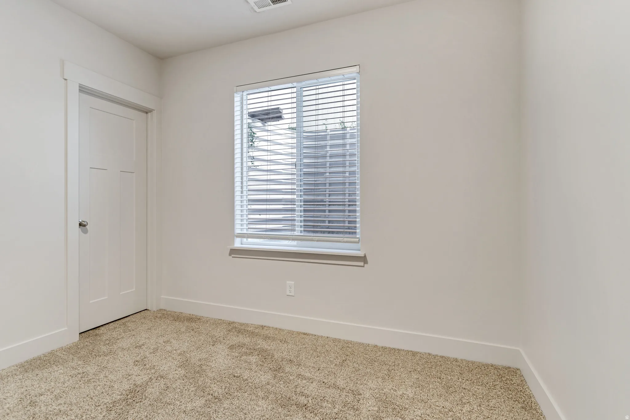 Neutral tone wall paint with a window featuring horizontal blinds, white trim, and a paneled interior door with a round knob