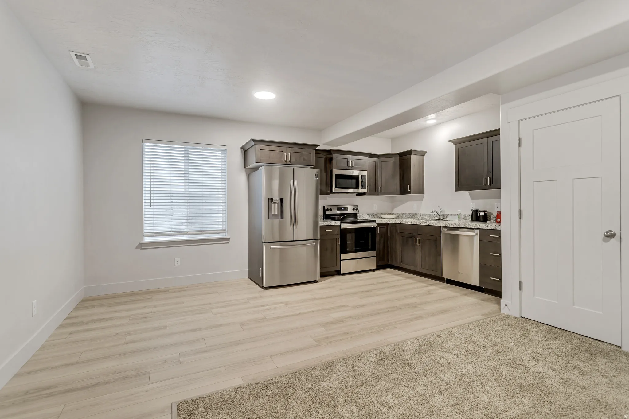 Kitchenette with wood-finish cabinetry, stainless steel appliances, and a light-toned countertop