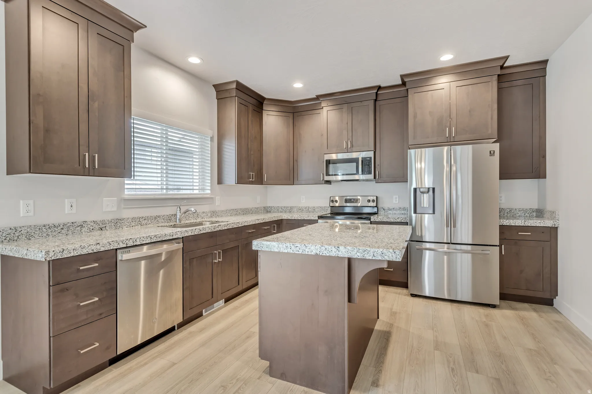 U-shaped kitchen featuring wood-finish cabinetry, granite countertops, stainless steel appliances, and a central island