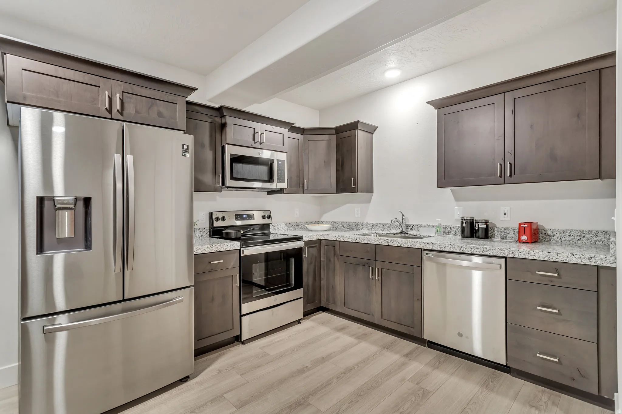 Kitchen featuring wood-finish cabinetry, stainless steel appliances, light-toned countertops, and wood-finish flooring