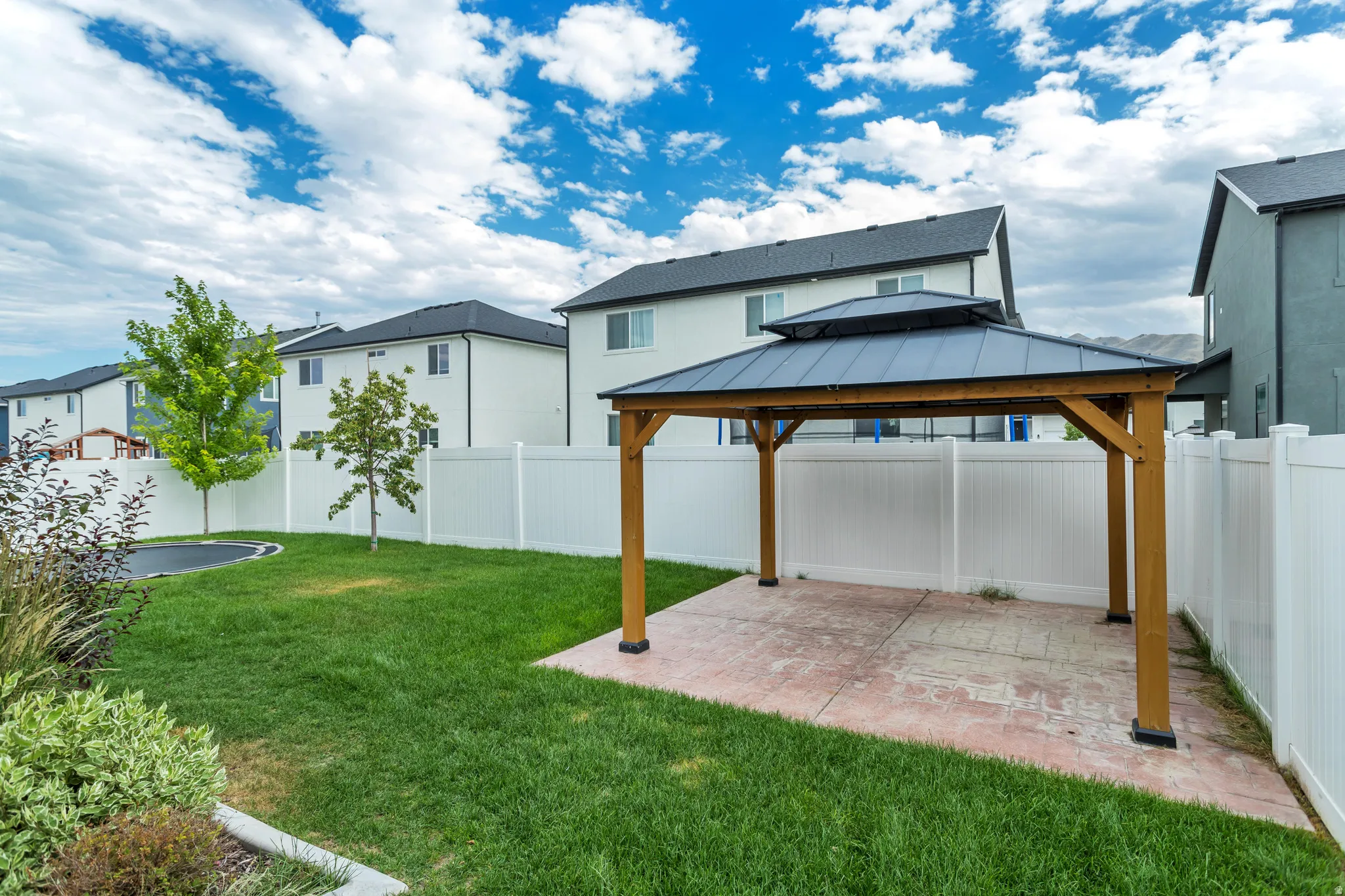 Expansive backyard featuring a lush lawn, mature trees, and a wooden gazebo with a metal roof