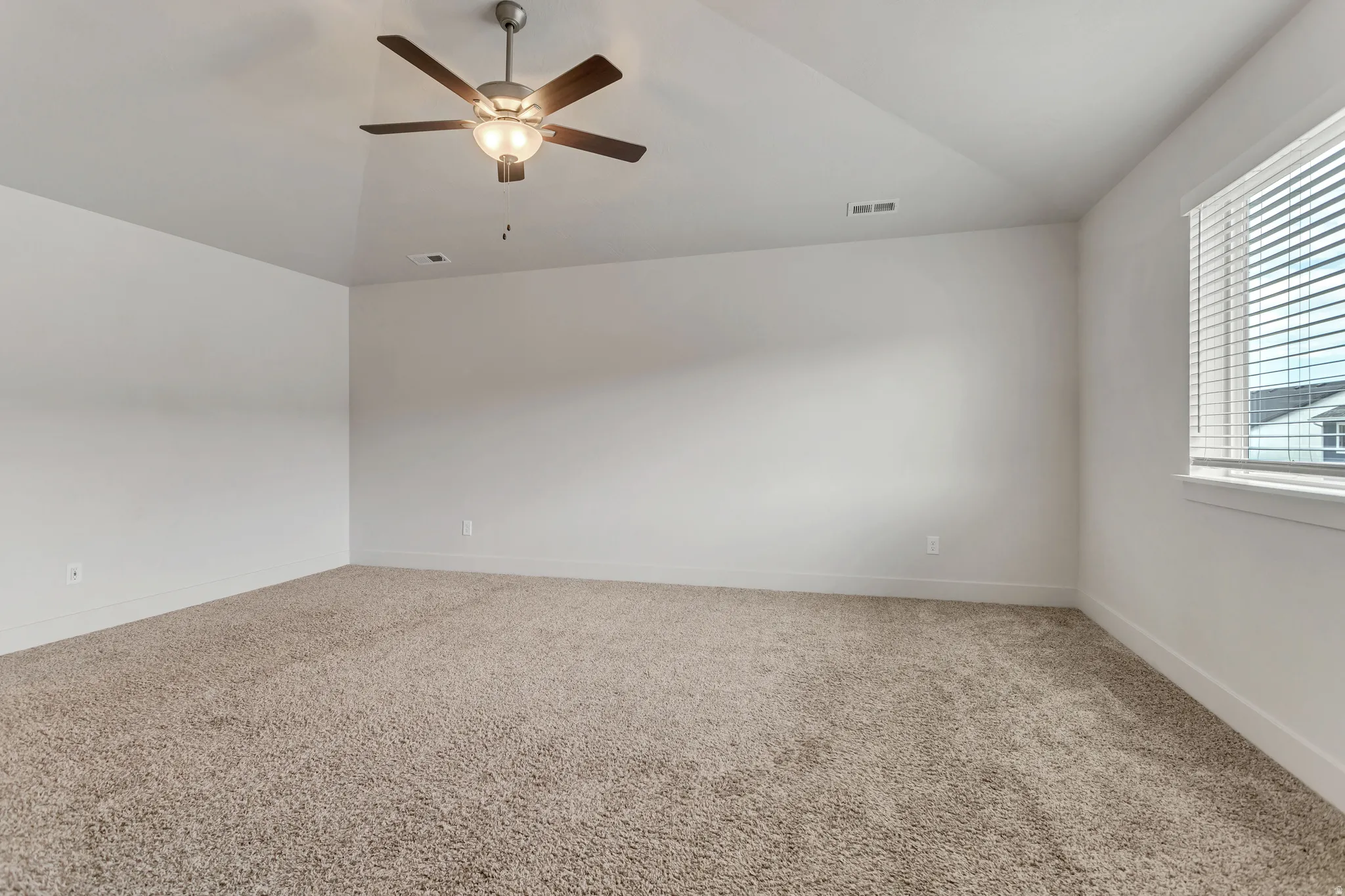 Neutral tone wall paint, carpeted flooring, window with blinds, and ceiling fan with integrated lighting