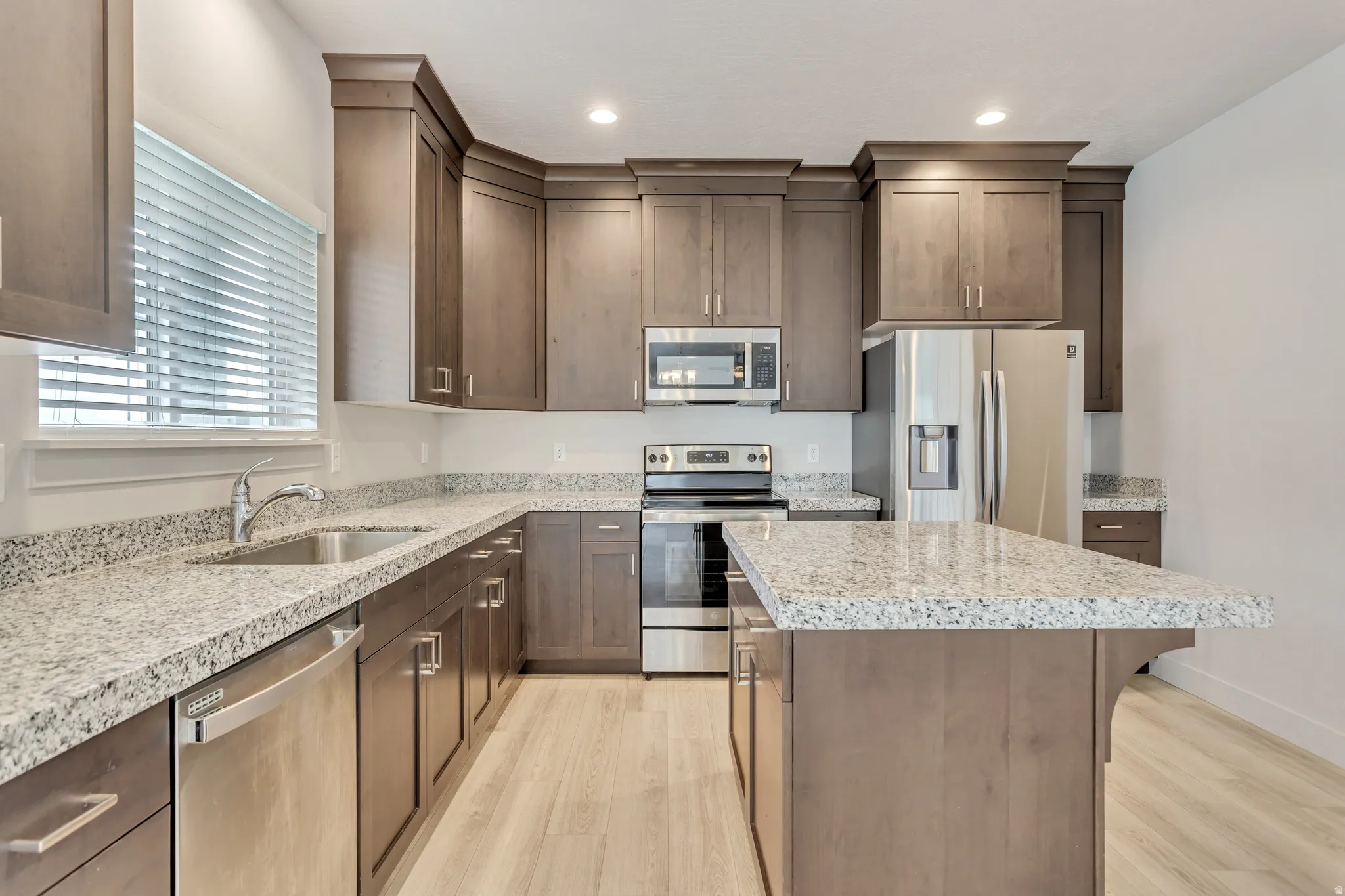 Kitchen featuring wood-finish cabinetry, light-toned countertops, stainless steel appliances, a center island, and wood-finish flooring