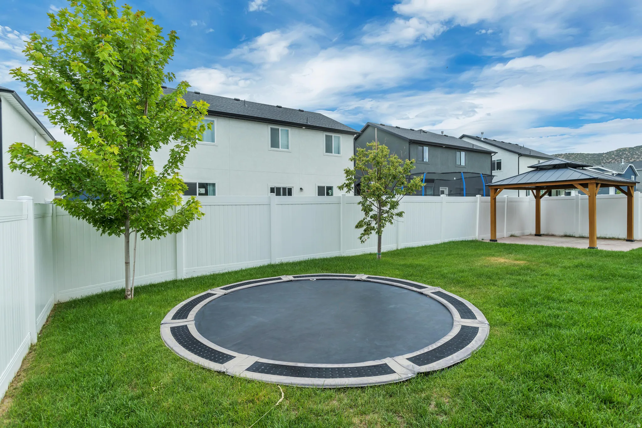 Expansive backyard featuring a manicured lawn, white privacy fencing, and a built-in gazebo with a layered roof design