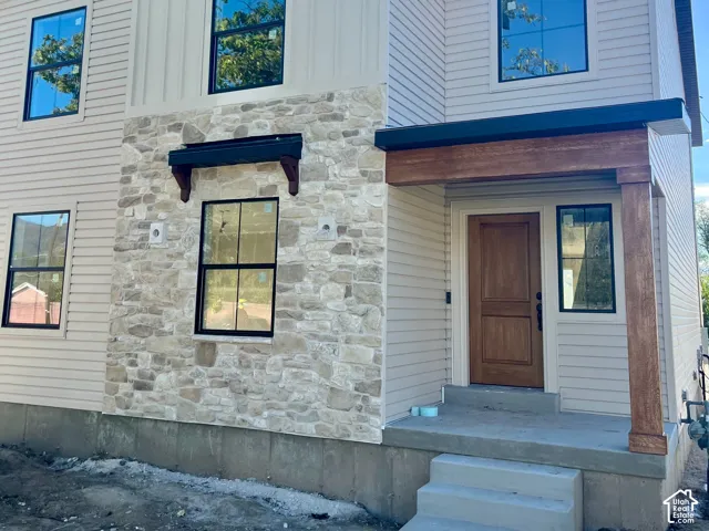 Modern exterior featuring a board and batten facade, horizontal siding, stone accents, black-framed windows, and a wood entry door