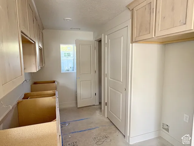 Unfinished kitchen featuring light wood-finish cabinetry, a single window, and multiple doors