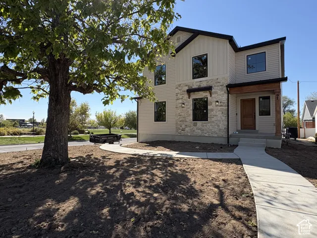 Contemporary exterior featuring light-colored siding, a prominent stone facade, black-framed windows, and a wood-finish entry door