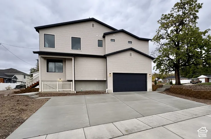 Two-story exterior featuring light-toned horizontal siding, a dark-toned two-car garage door, concrete driveway, and tiered stone retaining walls