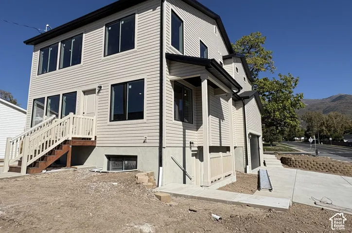 Light-toned siding with black-framed windows, multi-level exterior access, covered front entry porch, and an attached garage