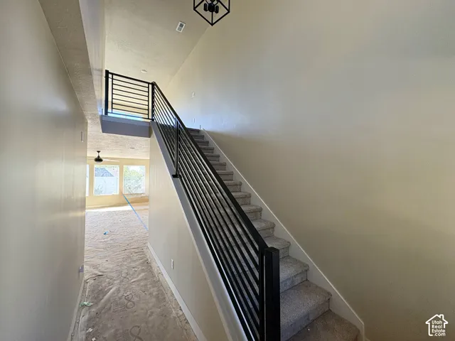 Staircase with horizontal bar railing, carpeted treads, and a high ceiling