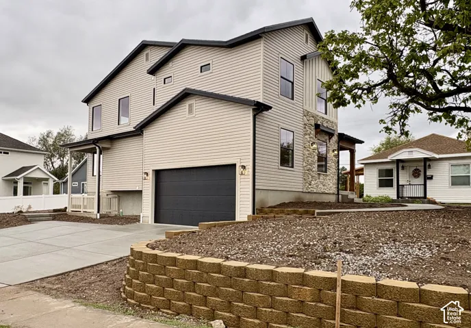 Multi-level exterior featuring light-toned horizontal siding, a stacked stone facade accent, a dark-toned garage door, and a tiered concrete retaining wall
