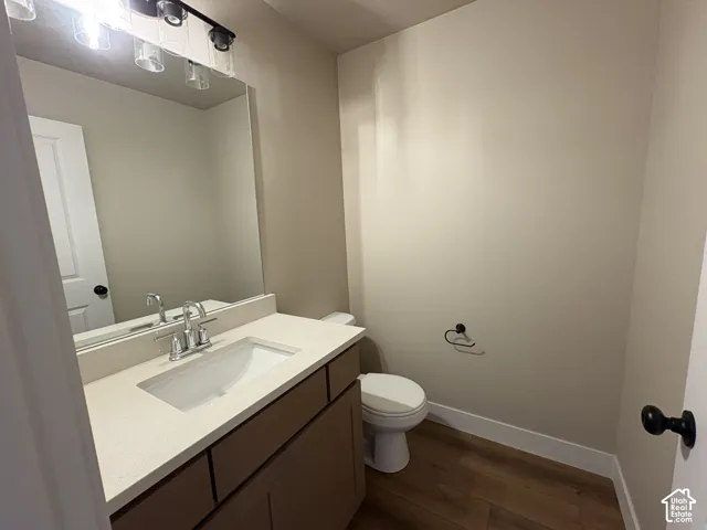 Bathroom featuring a neutral vanity with an integrated rectangular sink and stone-composite countertop, full-width vanity mirror, polished chrome faucet, and wood-finish flooring