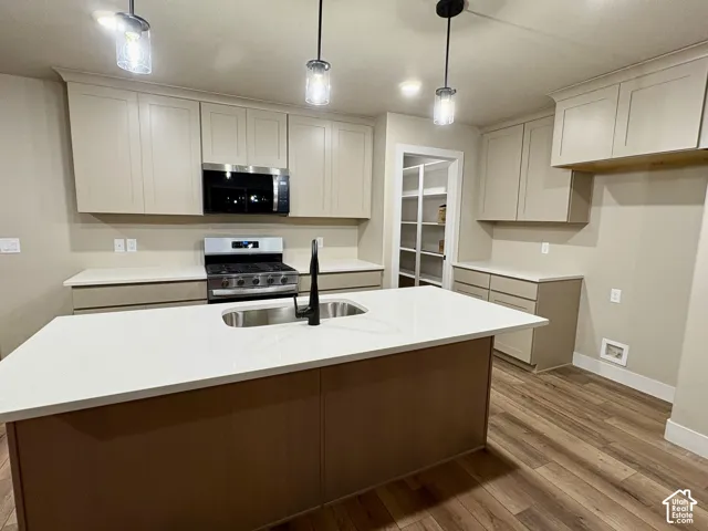 Kitchen featuring shaker-style cabinetry, a central island with a solid-surface countertop and undermount sink, matte black fixtures, stainless steel appliances, and wood-finish flooring