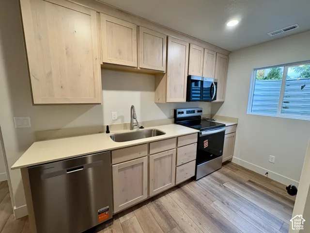 Kitchen featuring light wood-finish cabinetry, stainless steel appliances, solid surface countertops, and wood-finish flooring