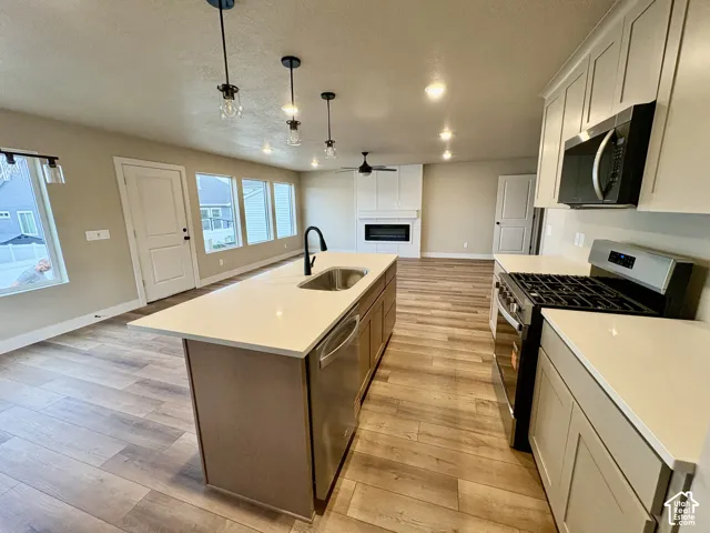 Kitchen featuring a center island with a stone-composite countertop, stainless steel appliances, shaker-style cabinetry, wood-finish flooring, and a recessed fireplace