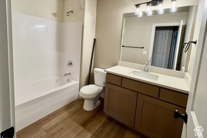 Bathroom featuring wood-finish flooring, vanity with a solid-surface countertop, rectangular undermount sink, multi-light fixture, and a tub-shower combination with a surround