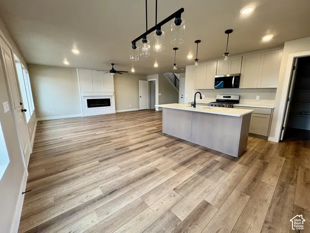 Open concept interior featuring wood-finish flooring, a kitchen island with quartz countertops, custom cabinetry, a built-in electric fireplace, and multi-light pendant fixtures