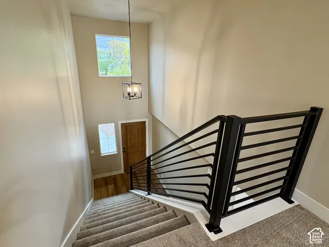Double-height foyer featuring a modern matte black metal railing, carpeted staircase, wood-finish front entry door, and a geometric pendant light fixture