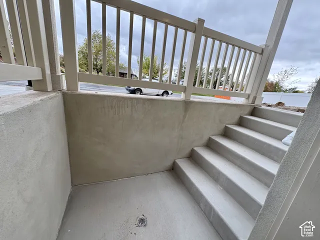 Concrete stairs with a concrete landing featuring a drainage grate, enclosed by a white railing system