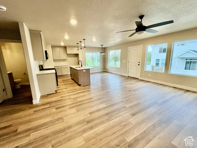 Open-concept kitchen featuring shaker-style cabinetry, a central island with a sink, wood-finish flooring, recessed lighting, and a ceiling fan