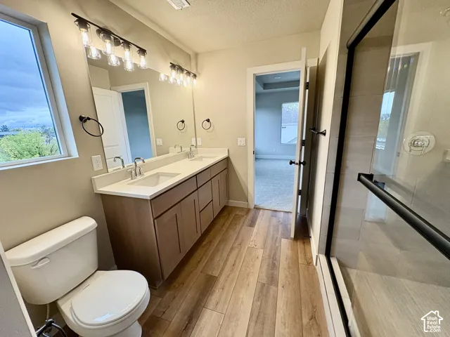 Bathroom featuring a double vanity with light wood-finish cabinetry, solid-surface countertop, industrial-style multi-bulb lighting, and a glass-enclosed shower with tiled surround