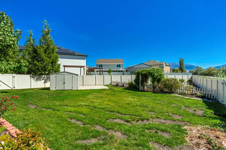 Expansive backyard with a manicured lawn, full privacy fencing, garden shed, concrete patio, and a decorative garden archway