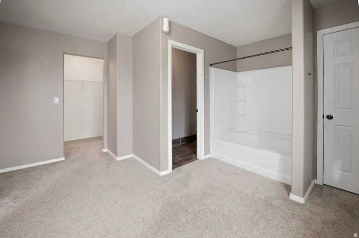 Light-colored carpeting throughout, full bathtub with shower surround, walk-in closet with wire shelving, and a panel door