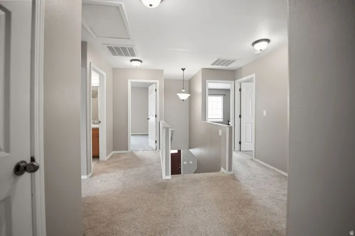 Carpeted hallway with painted walls, multiple entryways, and a staircase with railing