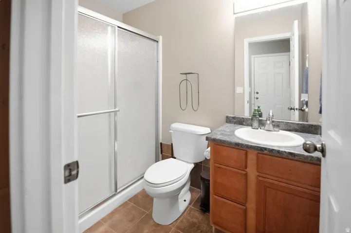 Vanity with wood-finish cabinetry and integrated sink, shower with sliding glass enclosure, and tile flooring