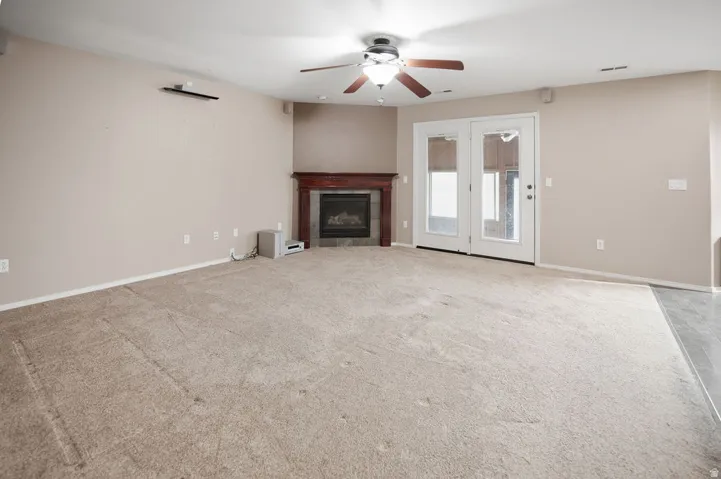 Recessed fireplace with wood mantel, ceiling fan with integrated lighting, and double glass-panel doors