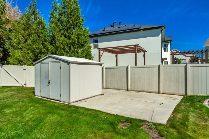 Expansive backyard featuring a manicured lawn, a concrete patio, and a utility shed with double doors
