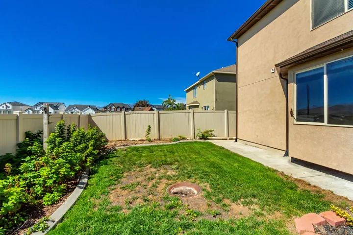 Expansive backyard featuring a manicured lawn, concrete pathway, and mature perimeter landscaping
