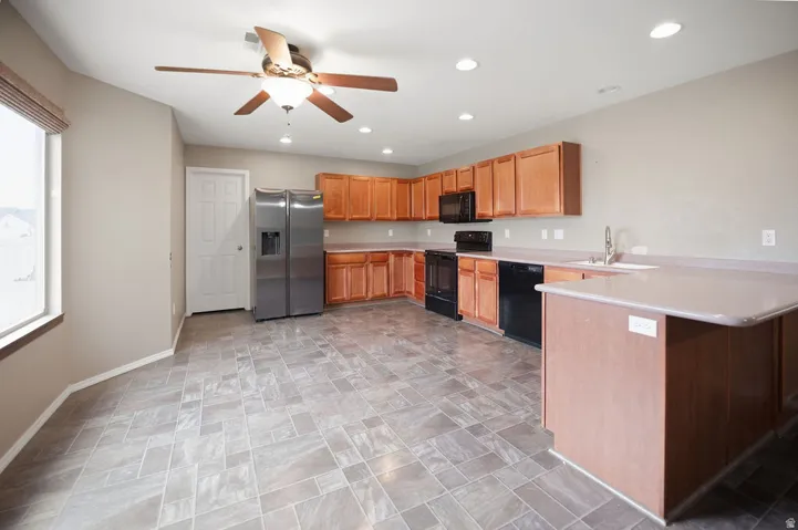 Kitchen featuring wood-finish cabinetry, stainless steel refrigerator, black range, black dishwasher, and a ceiling fan