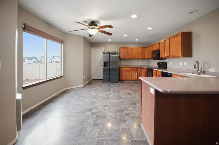 Open-concept kitchen and dining area featuring wood-finish cabinetry, stainless steel appliances, a kitchen island with an integrated sink, recessed lighting, and a ceiling fan