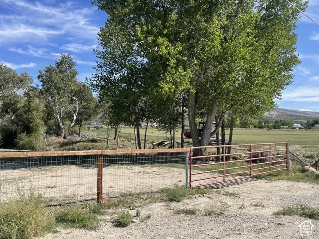 Fenced perimeter with a red metal gate, mature trees, and expansive open land