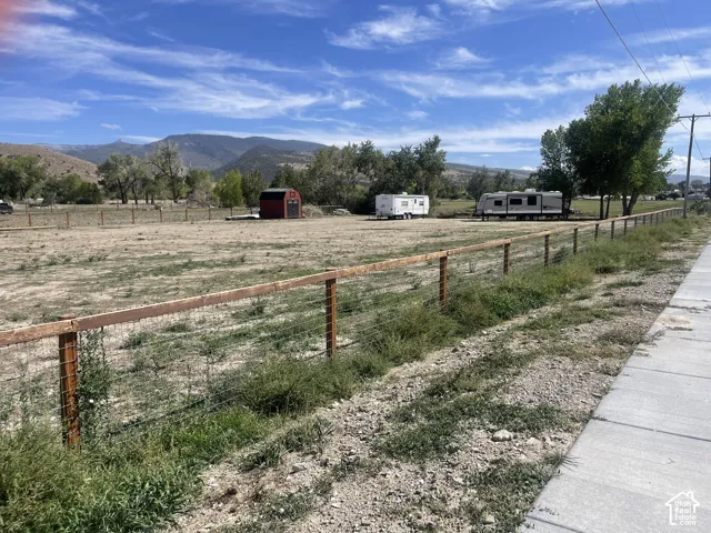 Expansive lot featuring a wood and wire fence, a small red shed, and a mountain backdrop