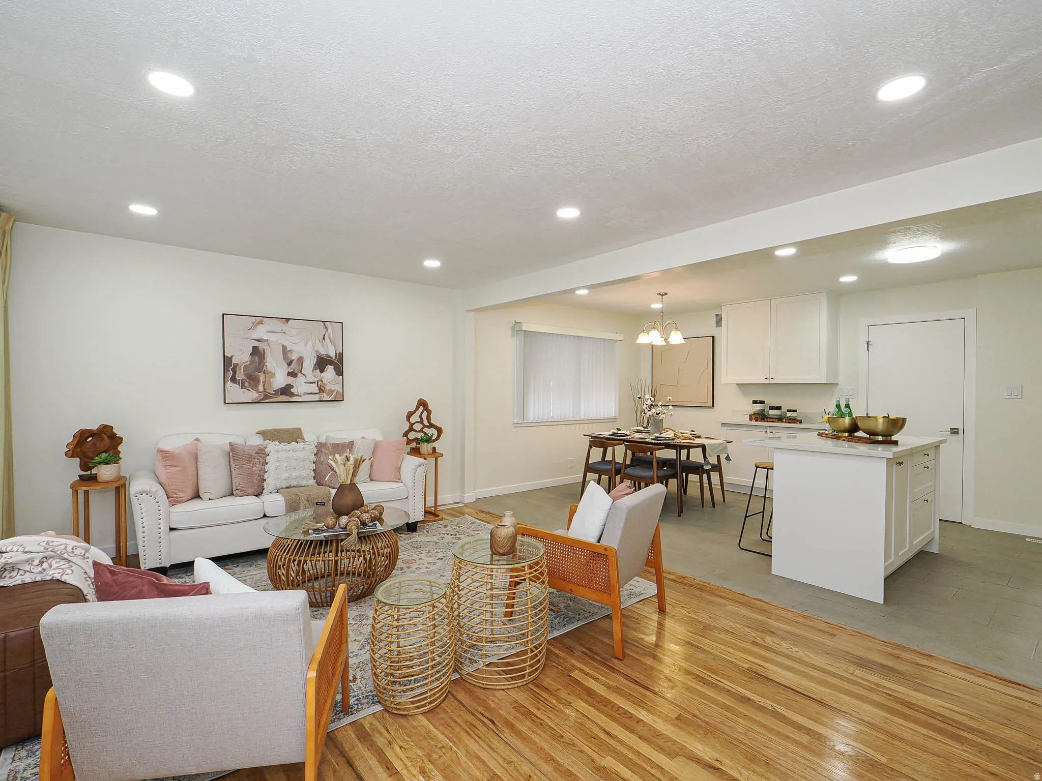 Recessed ceiling lighting, wood-finish flooring, white kitchen cabinetry, kitchen island with seating, and a dining area with chandelier