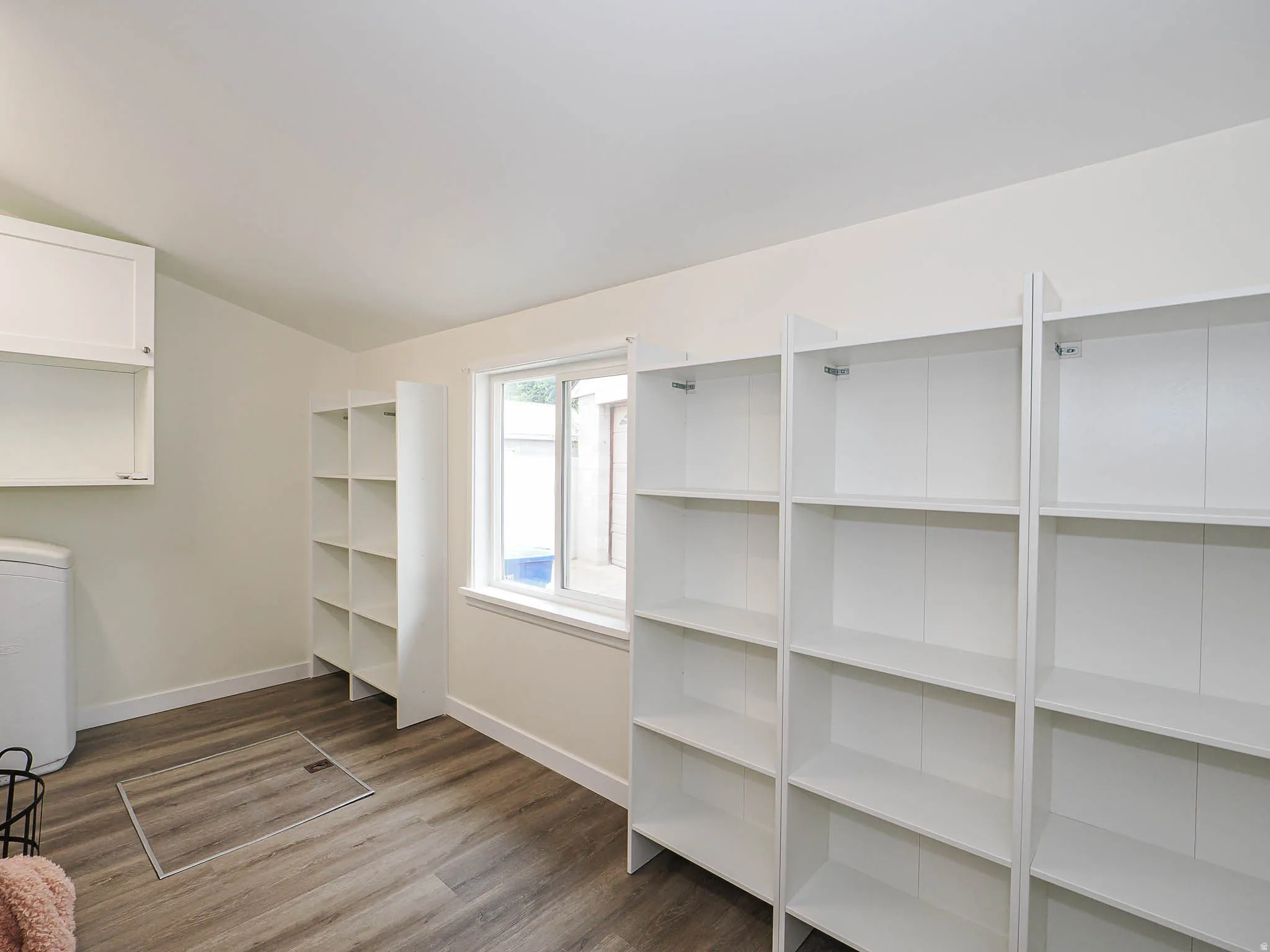 Wood-finish flooring, white walls, built-in shelving, white cabinetry, and a window