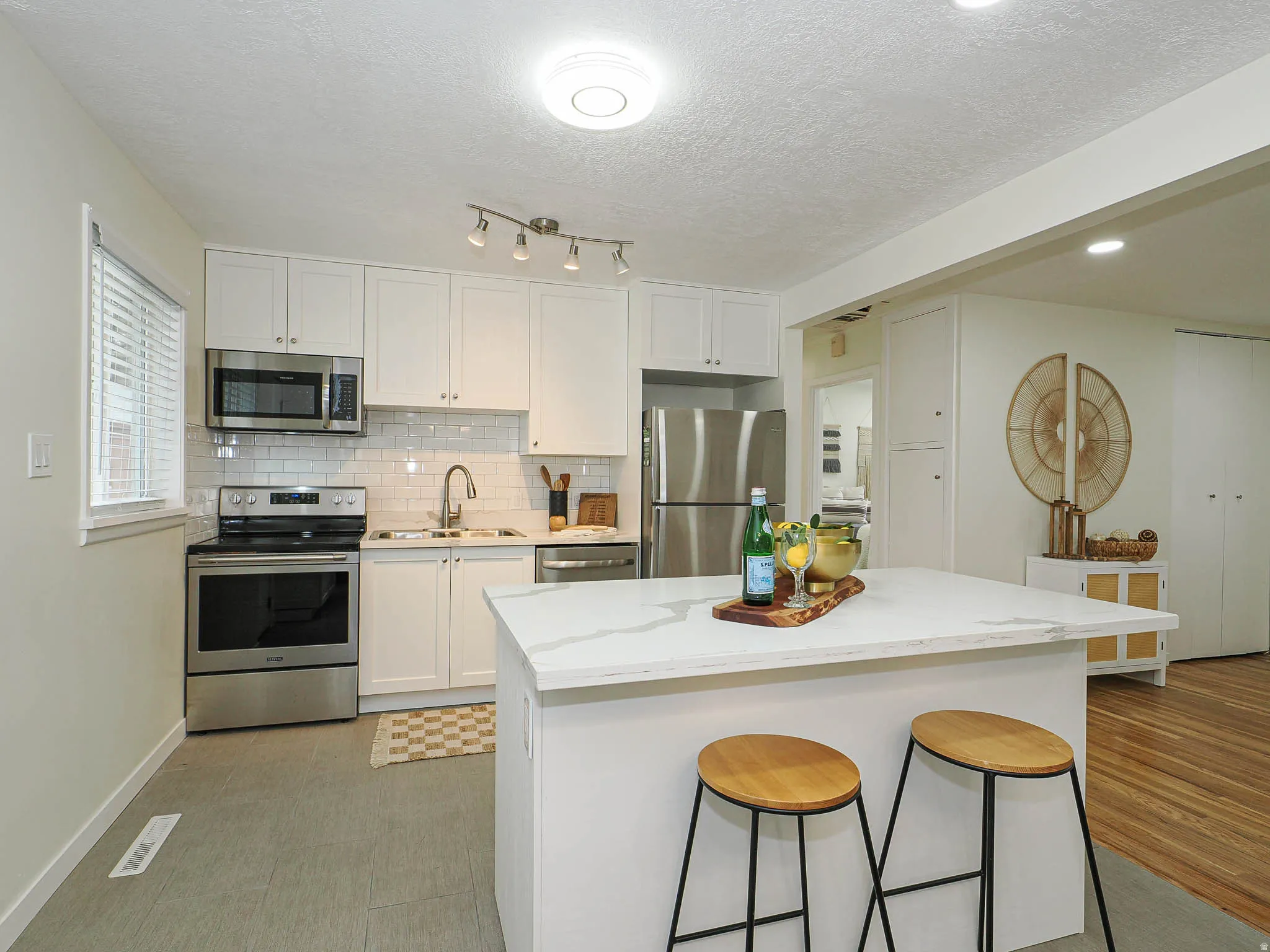 Kitchen featuring white cabinetry, stainless steel appliances, subway tile backsplash, and a central island with a light-toned countertop