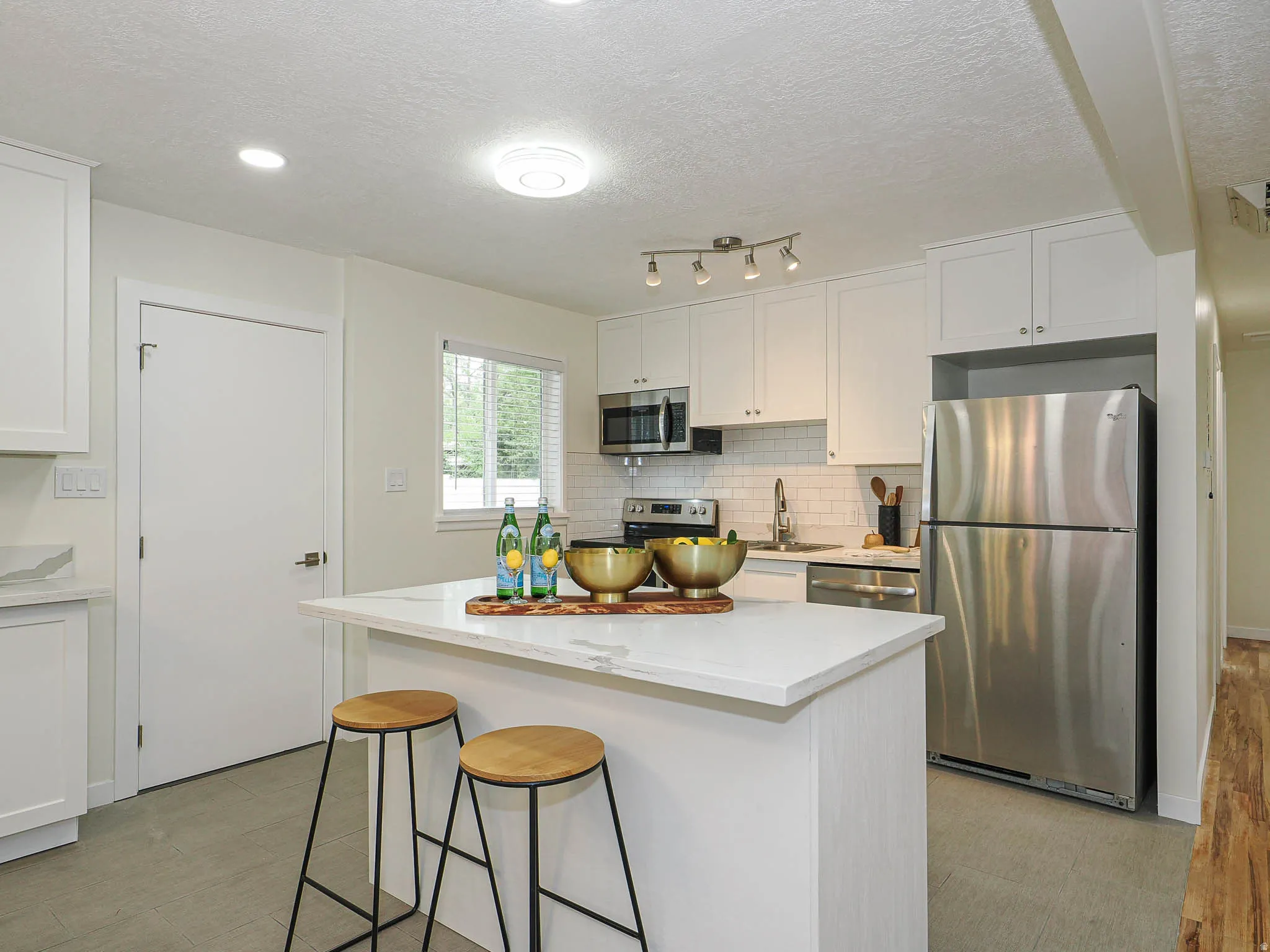 Renovated kitchen featuring white cabinetry, stainless steel appliances, a center island with a light-colored countertop, white subway tile backsplash, and recessed lighting