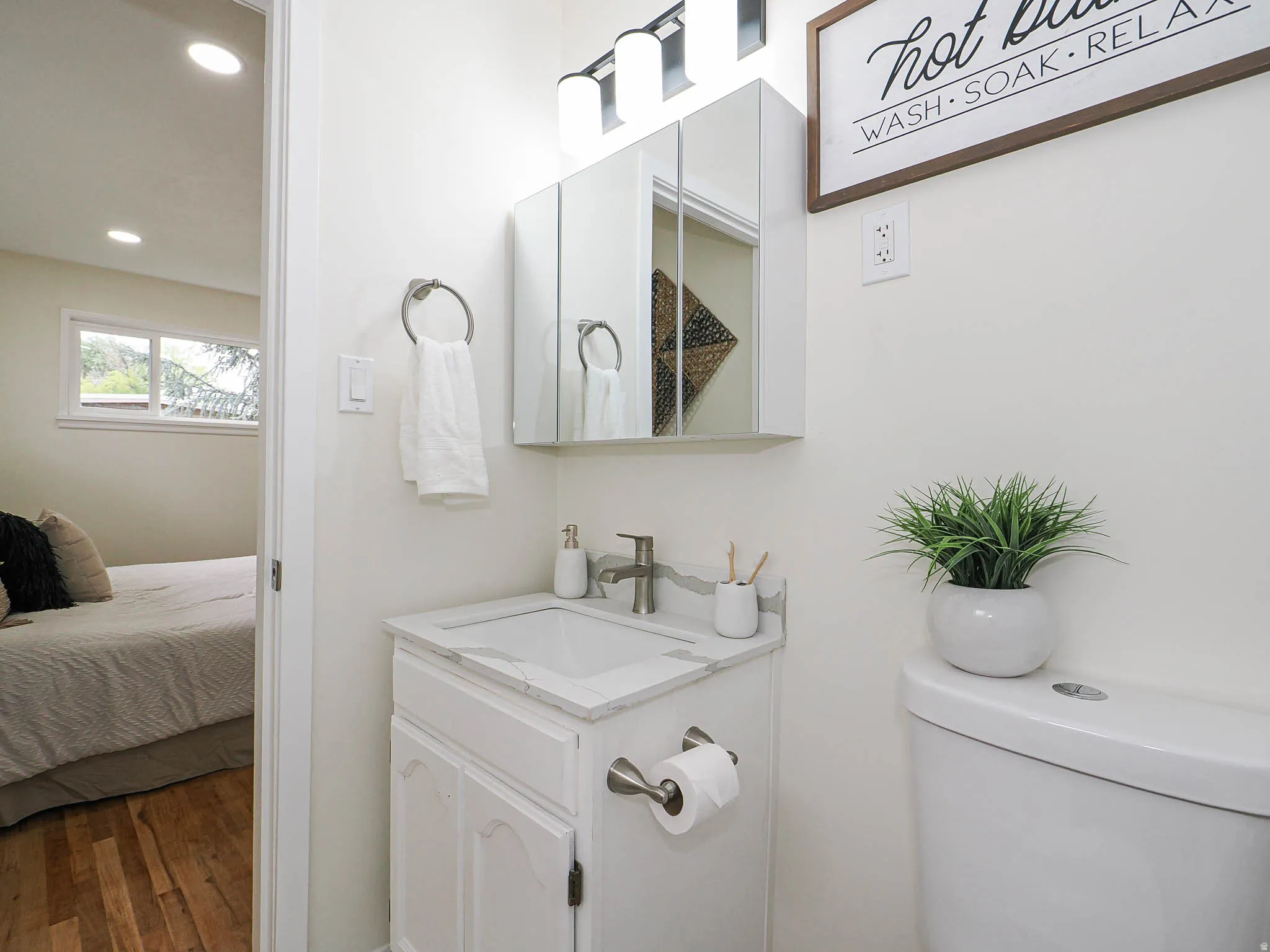 White vanity with integrated sink, wall-mounted mirrored medicine cabinet, and three-light bath fixture