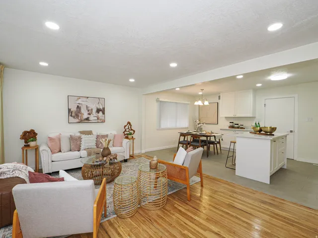 Recessed ceiling lighting, wood-finish flooring, white kitchen cabinetry, kitchen island with seating, and a dining area with chandelier