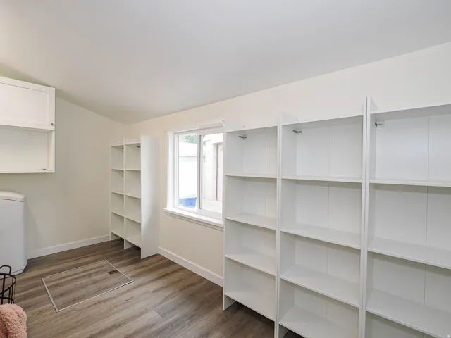 Wood-finish flooring, white walls, built-in shelving, white cabinetry, and a window