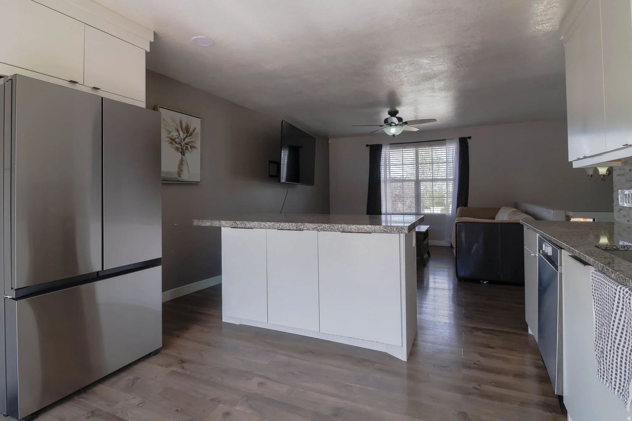Stainless steel French door refrigerator, kitchen island with stone countertop, wood-finish flooring, white cabinetry, and recessed lighting