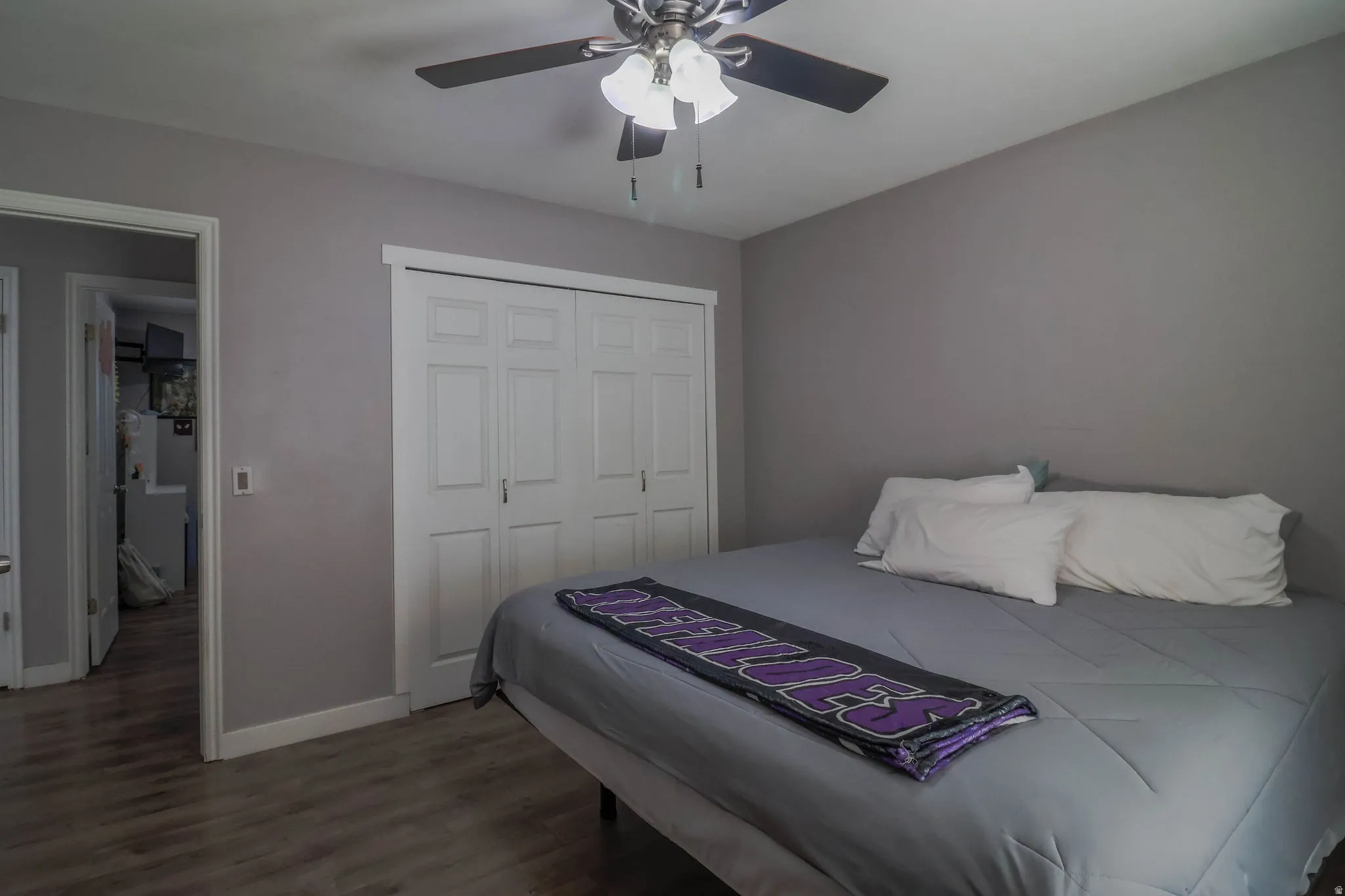 Wood-finish flooring, ceiling fan with integrated lighting, neutral wall palette, and bi-fold closet doors