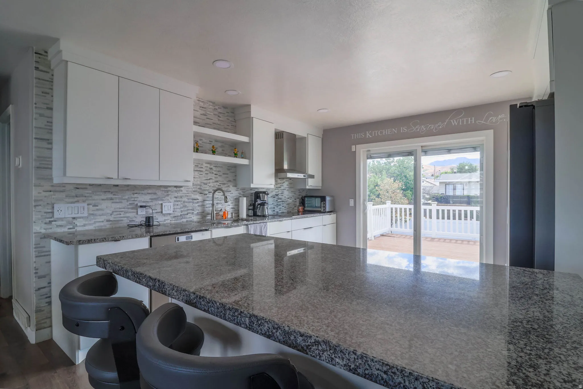Kitchen featuring an expansive island with a stone countertop, white cabinetry, a tile backsplash, recessed lighting, and sliding glass doors opening to a deck with white railings