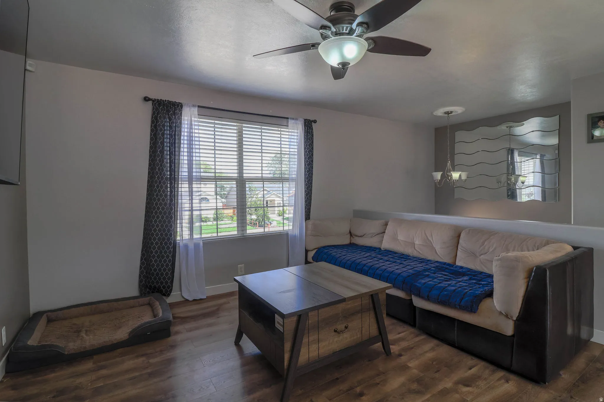 Wood-finish flooring, ceiling fan with integrated lighting, window with blinds, and built-in partial wall